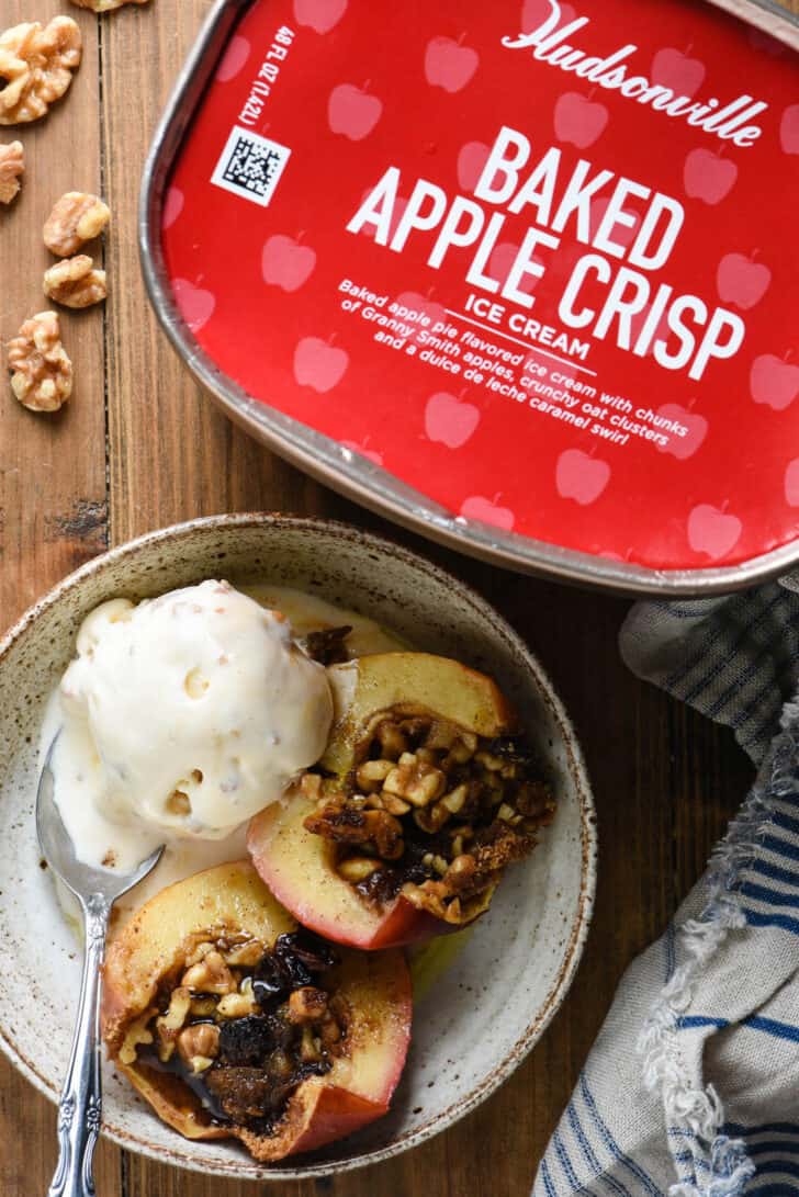 A carton of Hudsonville Baked Apple Crisp ice cream and a bowl of a stuffed baked apple with ice cream dessert.