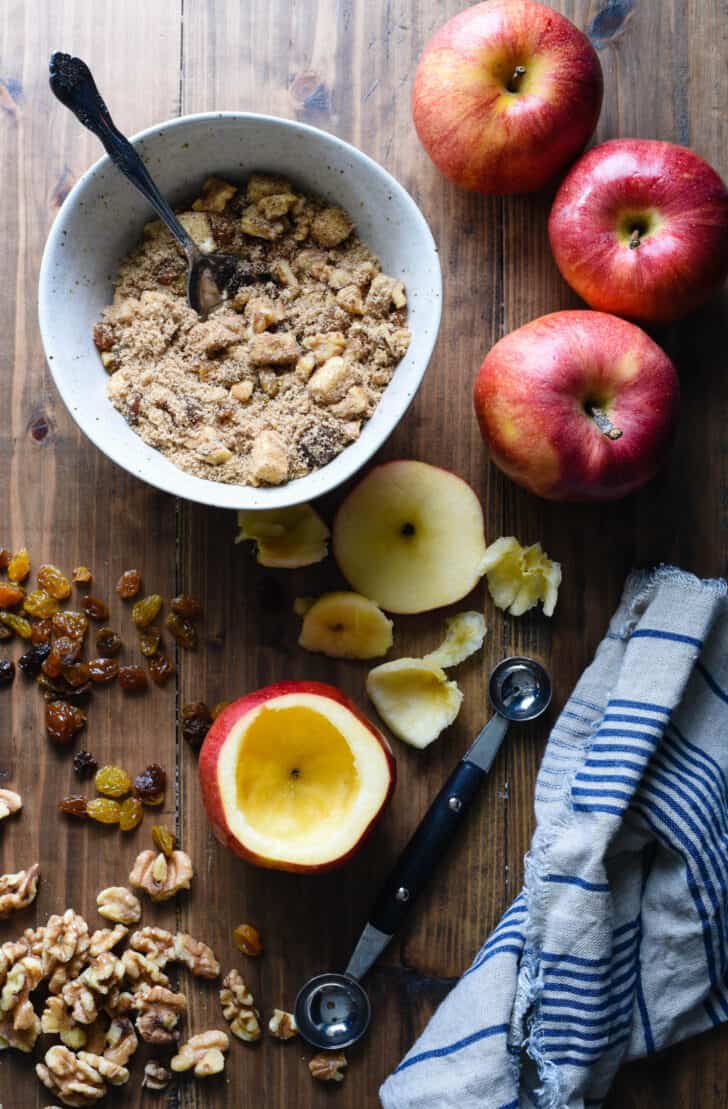 Ingredients for stuffed baked apples on a wooden table, including walnuts and raisins.