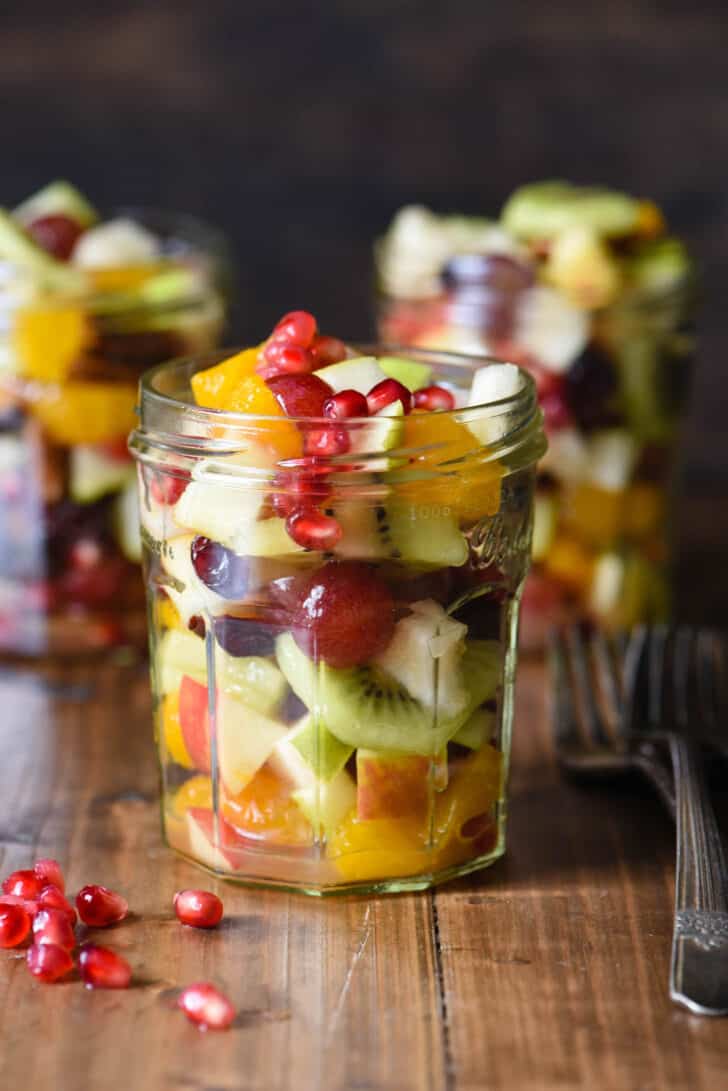 Small jam jar filled with autumn fruit salad made with grapes, pears, kiwi and pomegranate seeds, on a wooden tabletop.