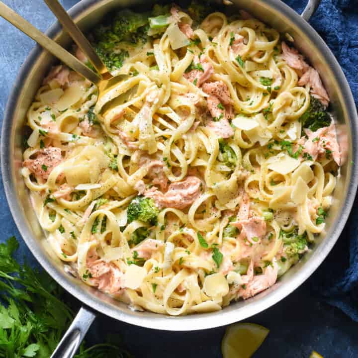A large stainless steel skillet filled with salmon alfredo pasta and broccoli.