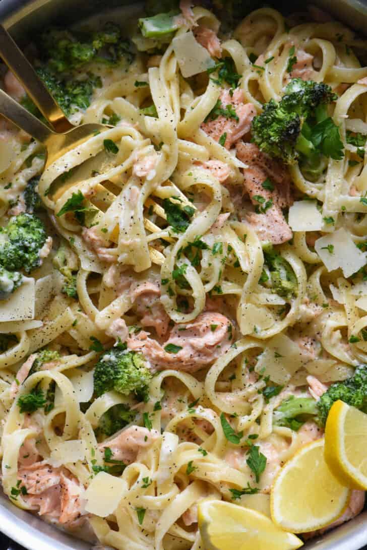 Closeup photo of salmon and broccoli alfredo pasta, with lemon wedge garnishes.