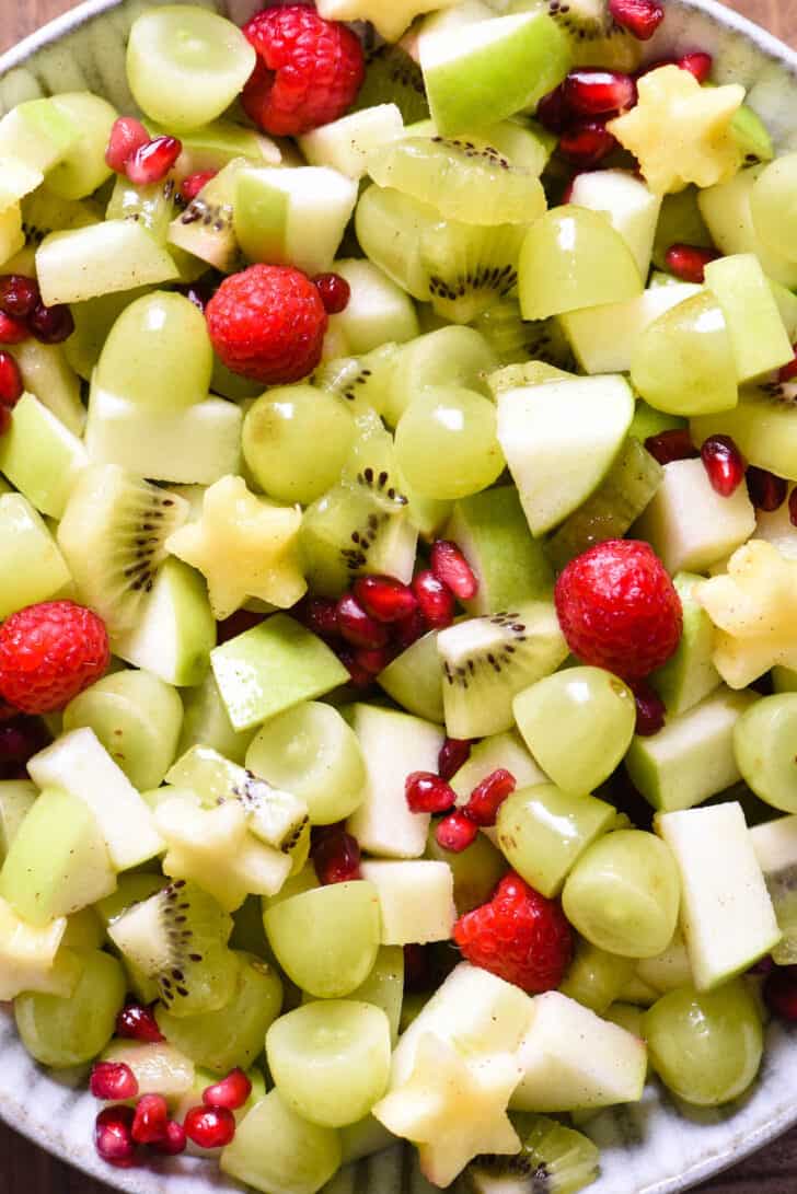 Green grapes, raspberries, pomegranate seeds, kiwi, green apple and star-shaped pineapple pieces tossed together.