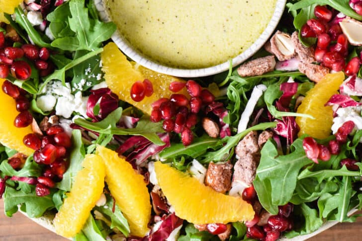 A salad for Christmas dinner made with greens, oranges, cheese, pomegranate seeds and nuts.