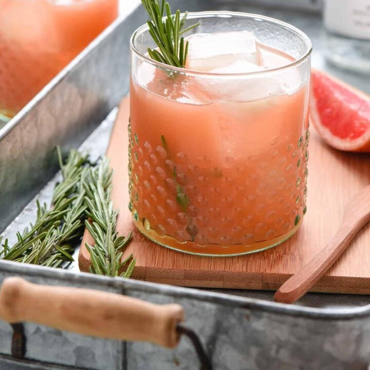 Grapefruit vodka cocktail with a rosemary sprig garnish in a textured glass on an aluminum tray.