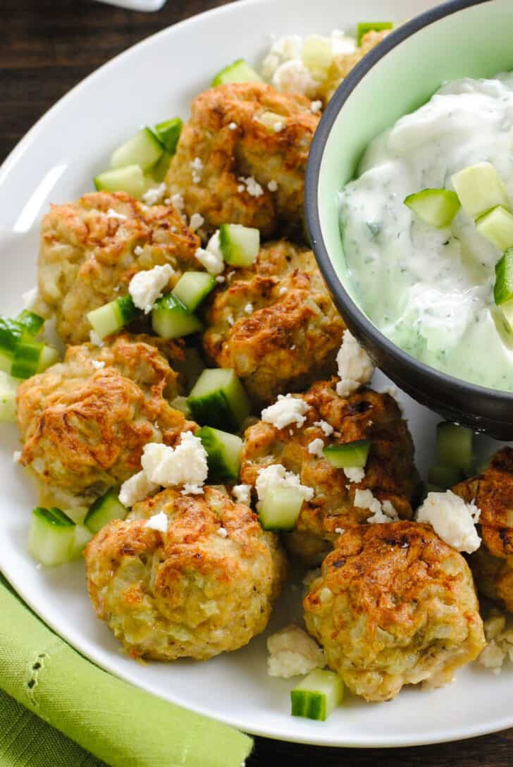 Closeup on baked chicken balls garnished with feta cheese and chopped cucumber.