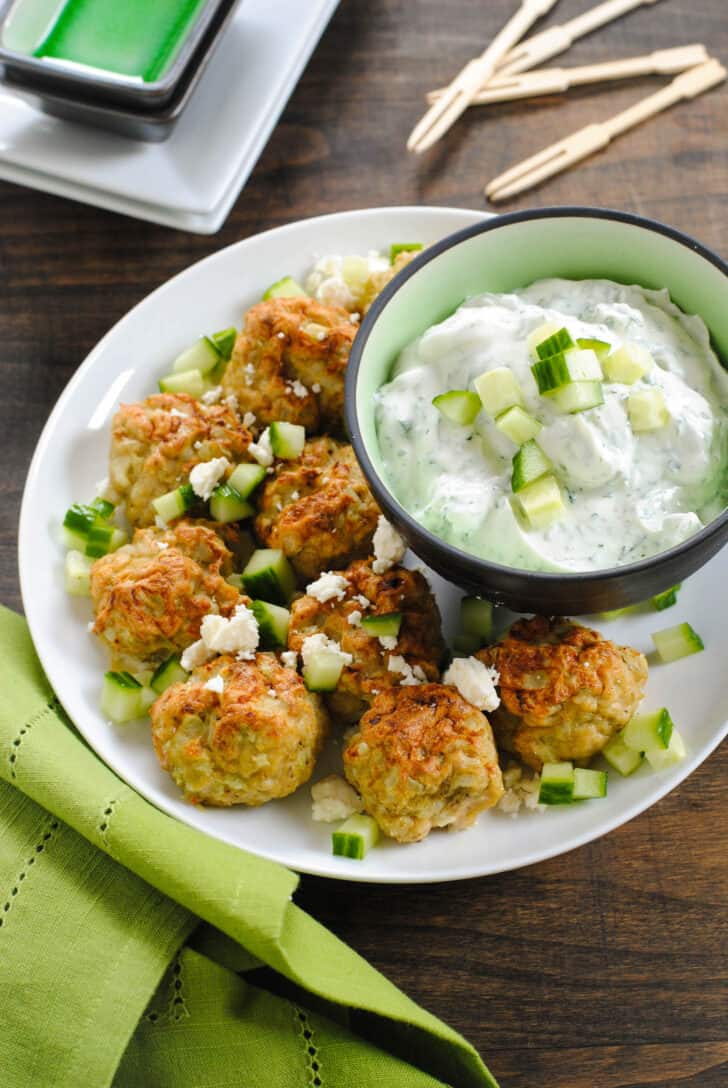 White plate topped with Greek chicken meatballs and a small bowl of yogurt dipping sauce.