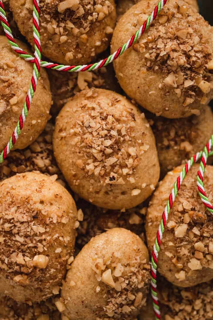 Greek honey cookies sprinkled with walnuts with a Christmas colored ribbon draped over them.
