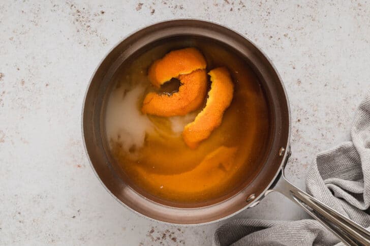 A saucepan filled with sugar, water and orange peels.