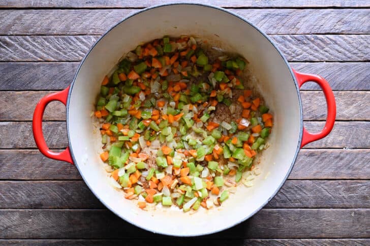 A red Dutch oven filled with sauteed mirepoix.