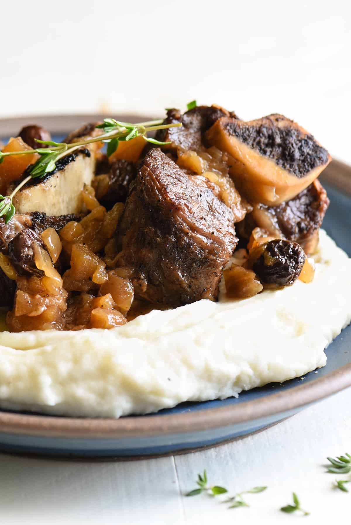 Shallow blue bowl filled with mashed potatoes, topped with Instant Pot short ribs and garnished with thyme.