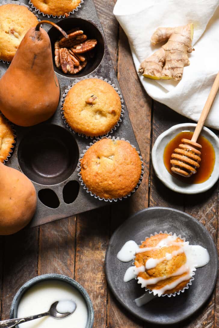 A baking pan full of pear muffins, with one on a plate topped with glaze.