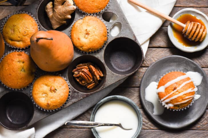 A baking pan full of pear muffins, with one on a plate topped with glaze.