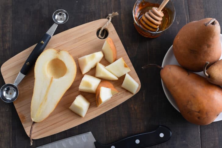 A small cutting board with a cut up pear on it, with a knife and melon baller alongside.