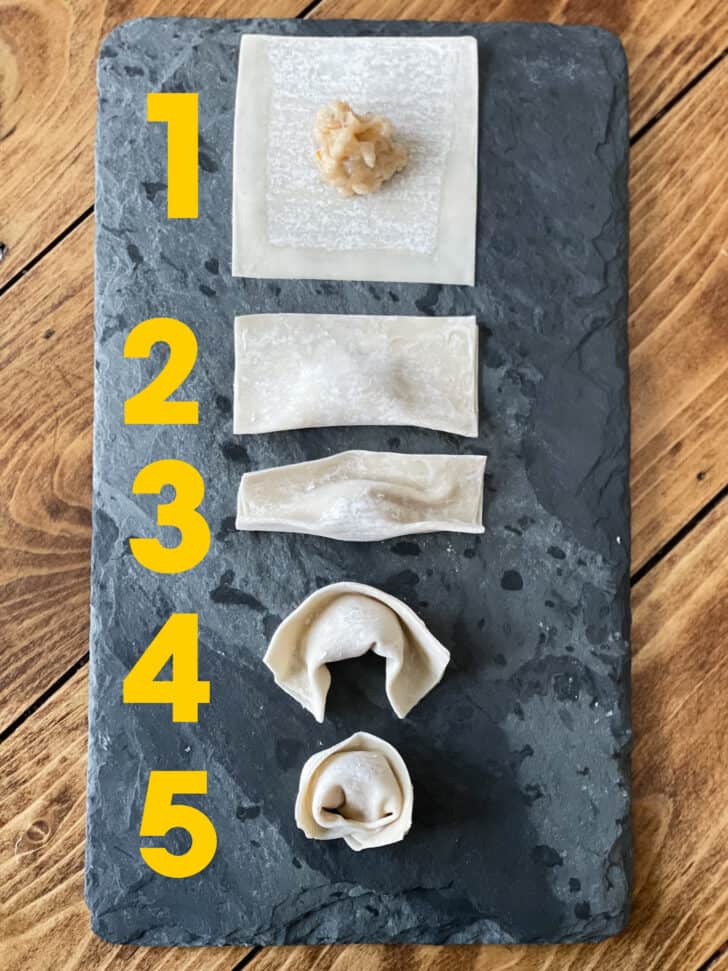 A slate board with numbered steps 1 through 5, showing how to fill and fold a shrimp wonton.