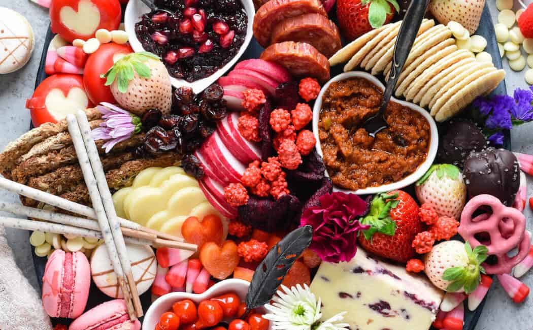 Large oval platter filled with red, pink and white Valentine's Day snacks, including cheese, charcuterie, fruits, vegetables, crackers and sweets.