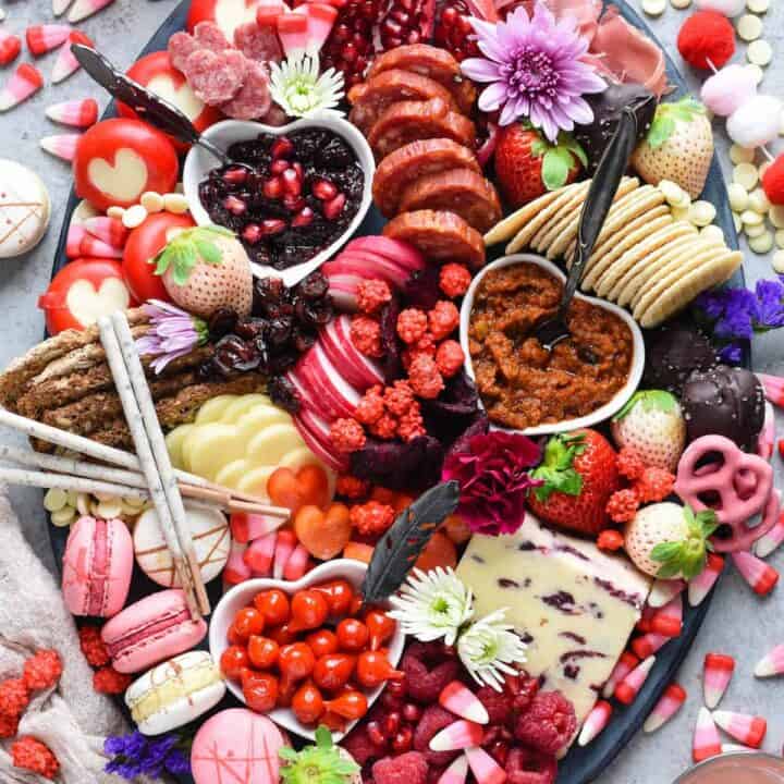 Large oval platter filled with red, pink and white Valentine's Day snacks, including cheese, charcuterie, fruits, vegetables, crackers and sweets.