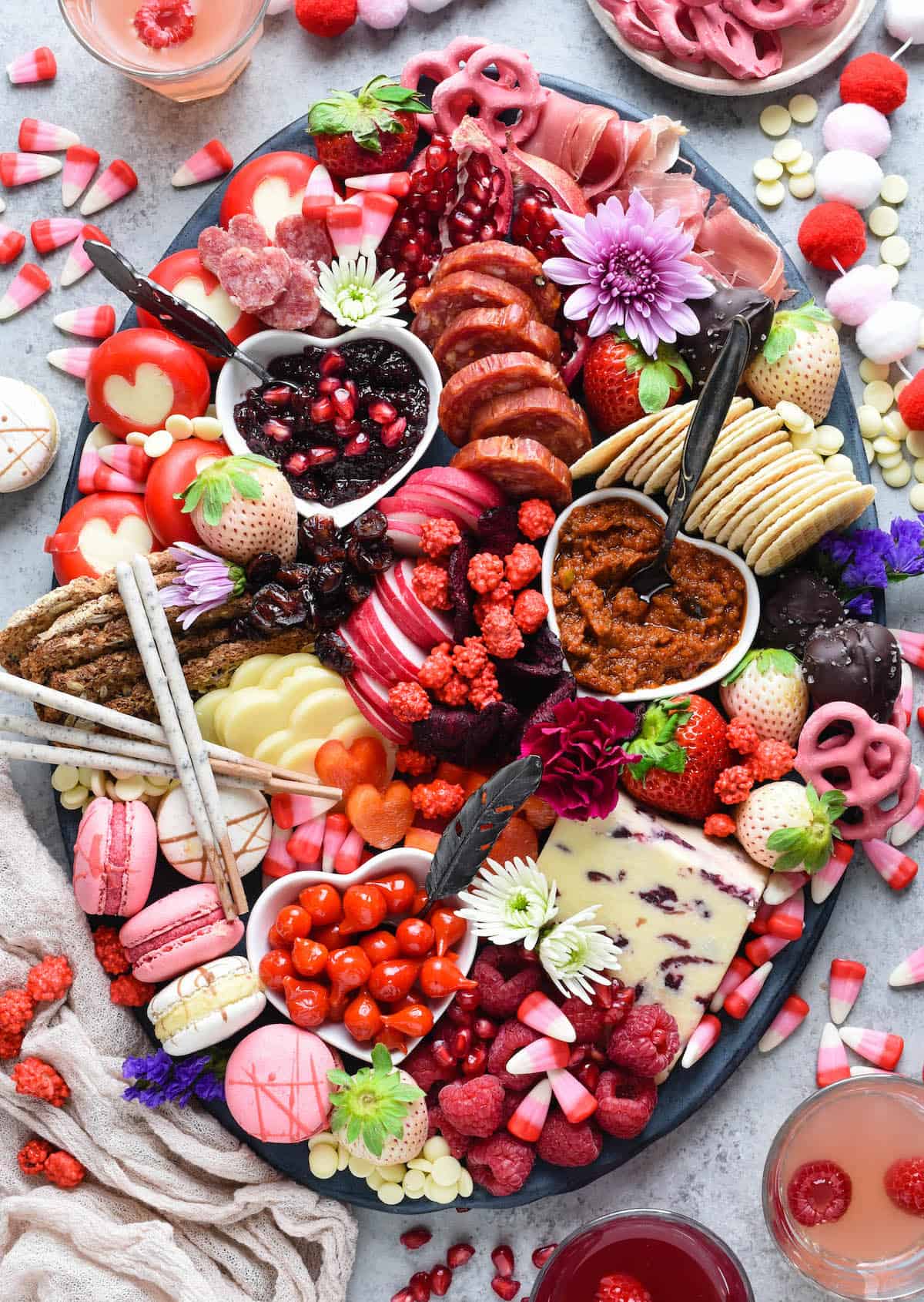 Large oval platter filled with red, pink and white Valentine's Day snacks, including cheese, charcuterie, fruits, vegetables, crackers and sweets.