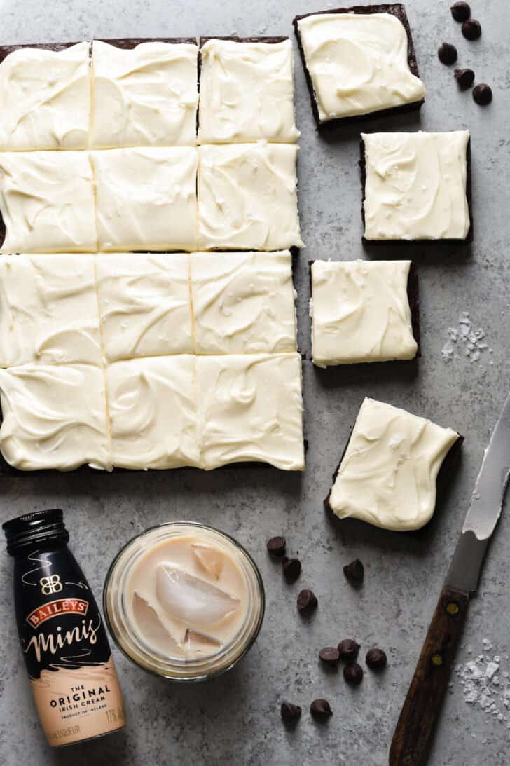 Baileys Irish Cream brownies, cut into squares, with a small bottle and glass of Baileys nearby.