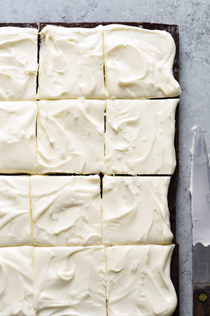 Irish cream chocolate dessert bars with cream cheese frosting, cut into squares, on a gray table with a knife.