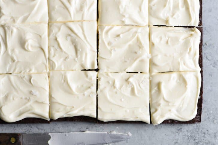 Irish brownies with cream cheese frosting, cut into squares, on a gray table with a knife.