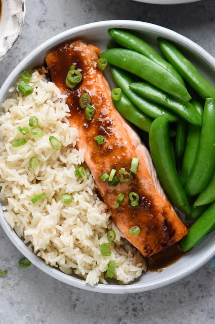 Closeup on plate of bourbon salmon, white rice and sugar snap peas.