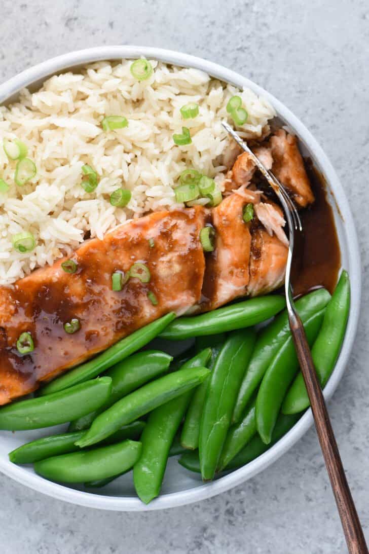 Closeup on plate of fish with brown sauce, white rice and sugar snap peas.