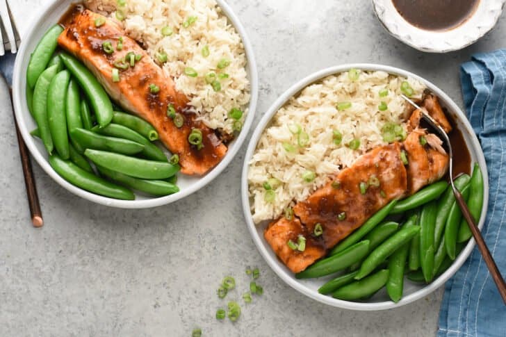 Two plates filled with fish with brown glaze, white rice garnished with green onions and sugar snap peas.