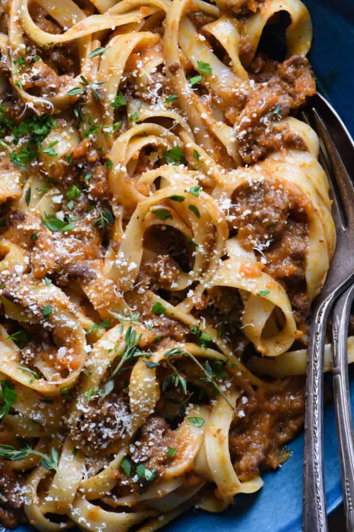 A closeup on pasta with meat sauce garnished with herbs and Parmesan cheese.