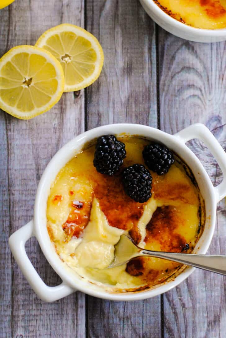 Round white ramekins with handles filled with eggy custard and topped with blackberries.