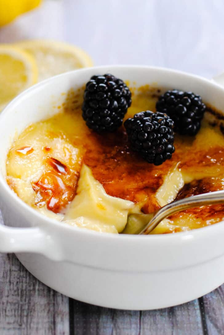 White ceramic bowl with handles, filled with lemon creme brulee and topped with blackberries.
