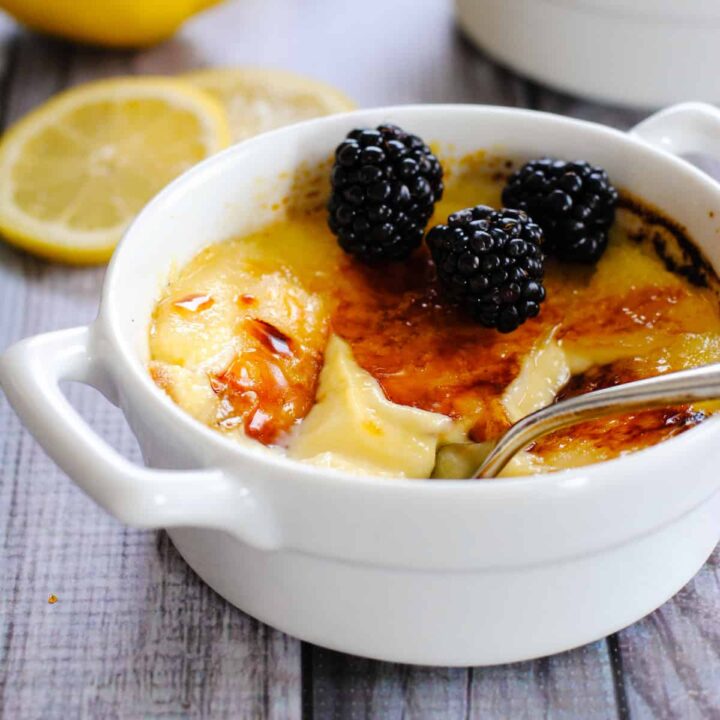 White ceramic bowl with handles, filled with lemon creme brulee and topped with blackberries.