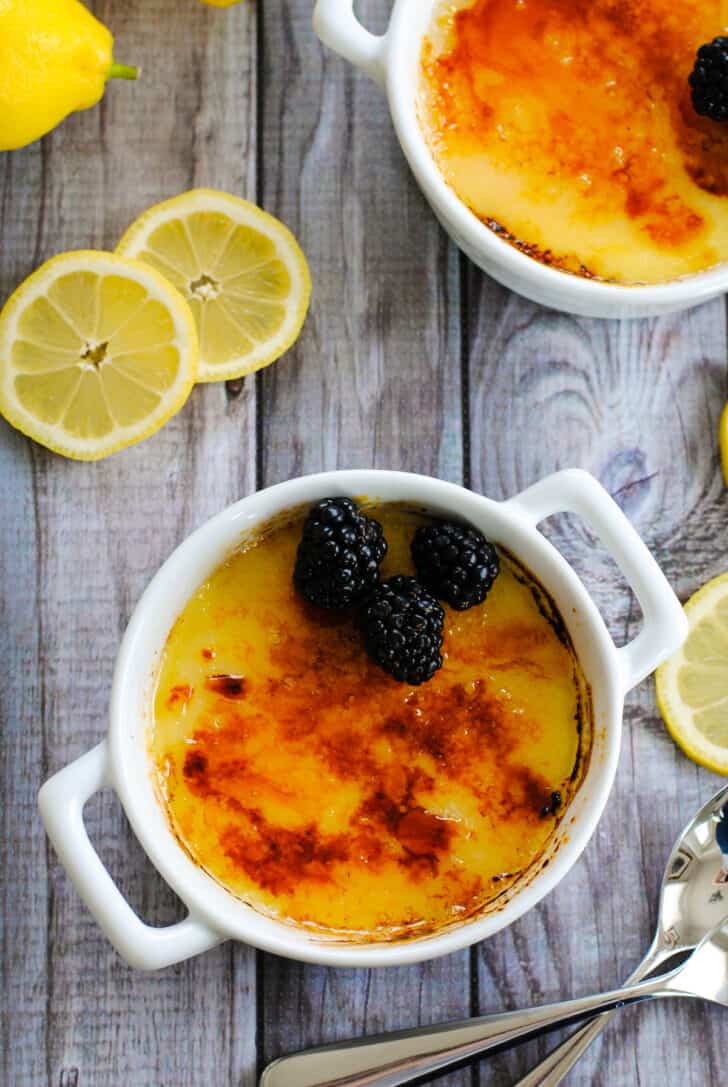 Two white ceramic ramekins filled with an easy lemon creme brulee recipe and topped with blackberries.