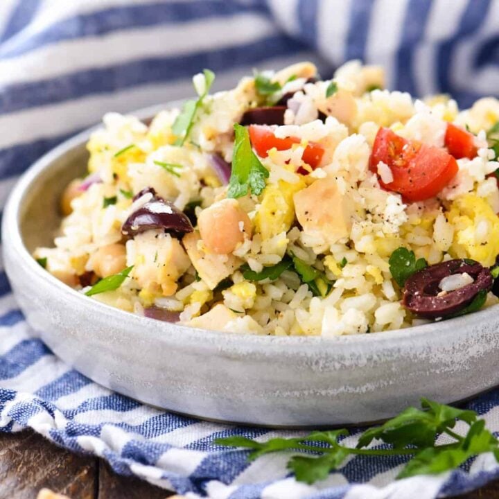 A shallow gray bowl filled with a Greek rice recipe containing chicken, vegetables, chickpeas and feta cheese.