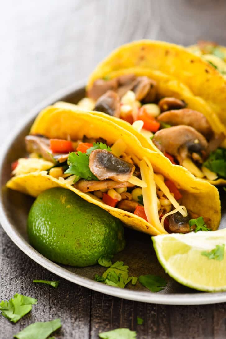 Mushroom tacos made in corn tortillas, on a tray with lime wedges and cilantro.
