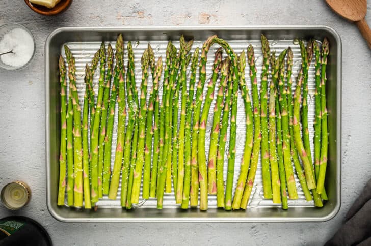 A rimmed baking pan with a row of fresh asparagus on it.
