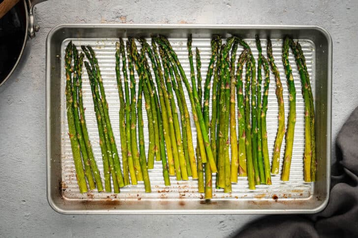 A rimmed baking pan with a row of cooked green vegetables on it.