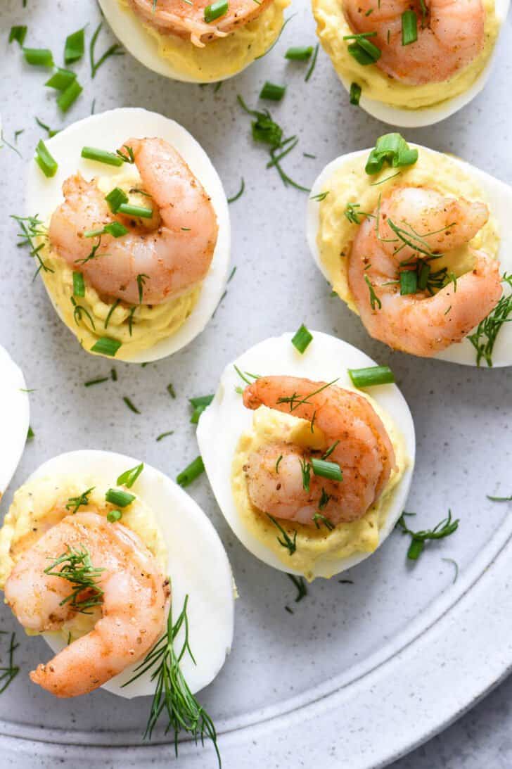 Shrimp deviled eggs served as Memorial Day appetizers on light gray plate, garnished with herbs.