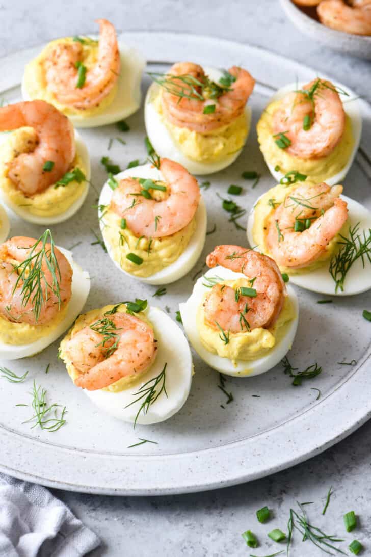 Shrimp deviled eggs garnished with chives and dill on a light gray plate.