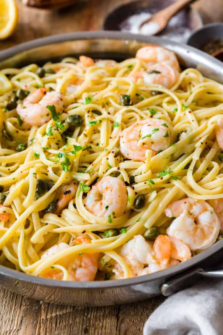 Stainless steel skillet filled with lemon pasta with capers and shrimp, garnished with parsley.