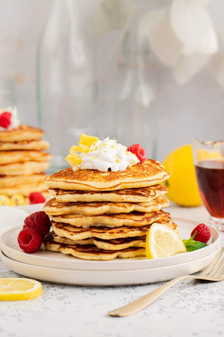 A stack of hotcakes garnished with berries, cream and citrus curls.