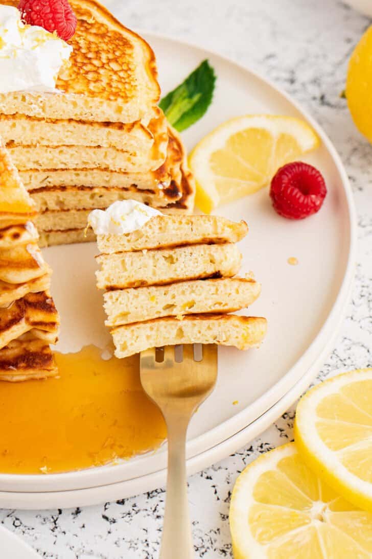 A fork removing a bite of a stack of lemon pancakes.