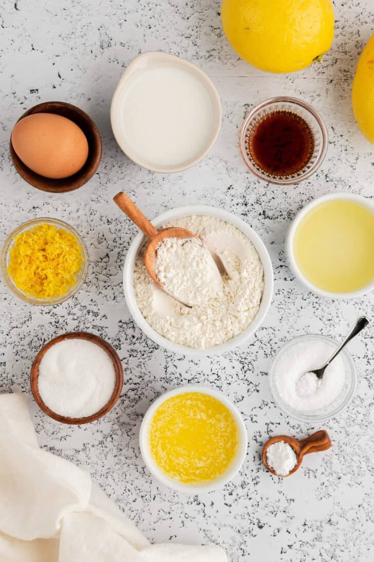 Small bowls of ingredients on a light background, including flour, milk, eggs, sugar and citrus zest and juice.