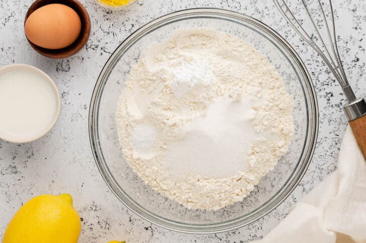 A glass mixing bowl filled with flour and other dry baking ingredients.