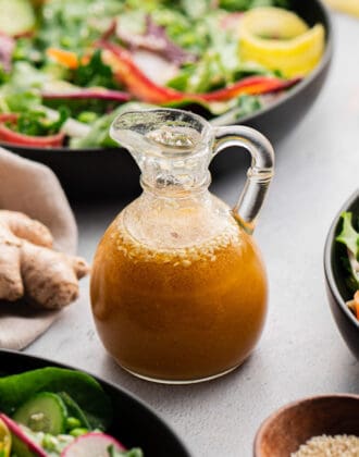 Miso ginger dressing in a small glass carafe, with a fresh vegetable salad in the background.