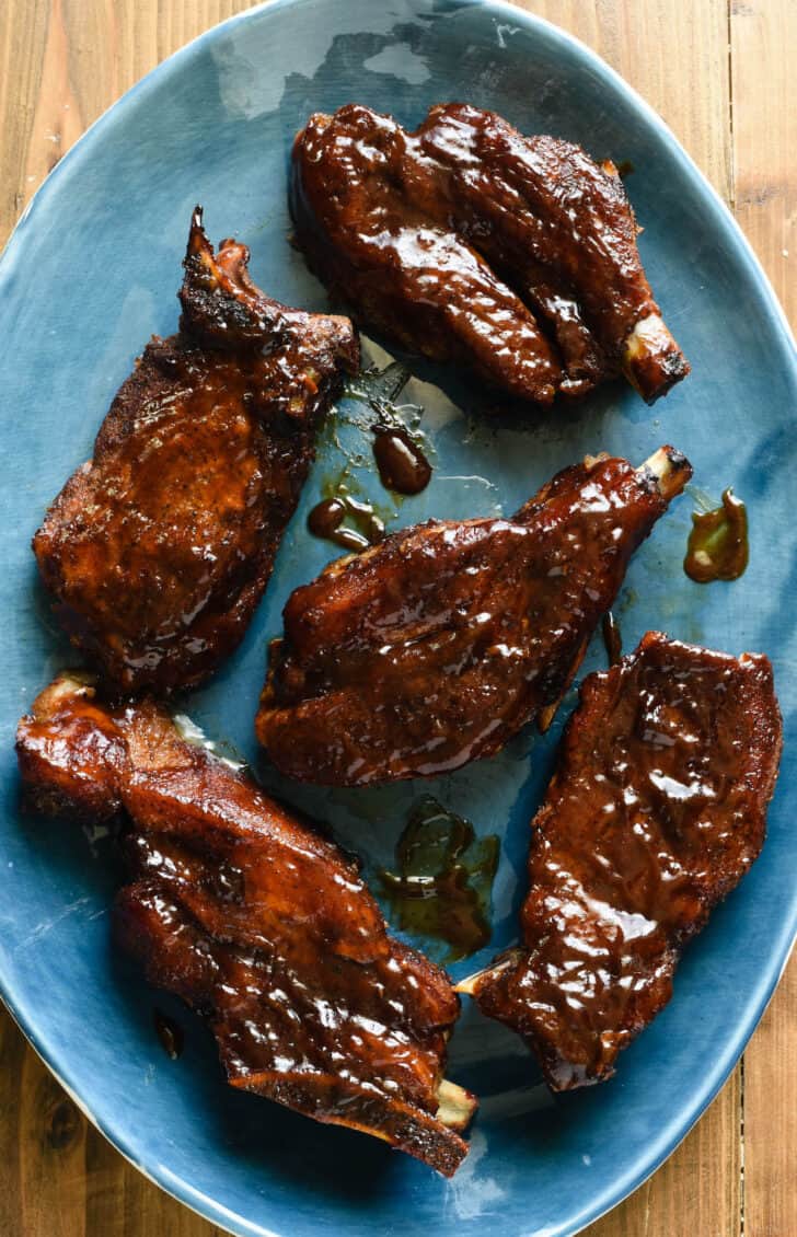 Country style pork ribs glazed with barbecue sauce on an oval shaped blue platter.