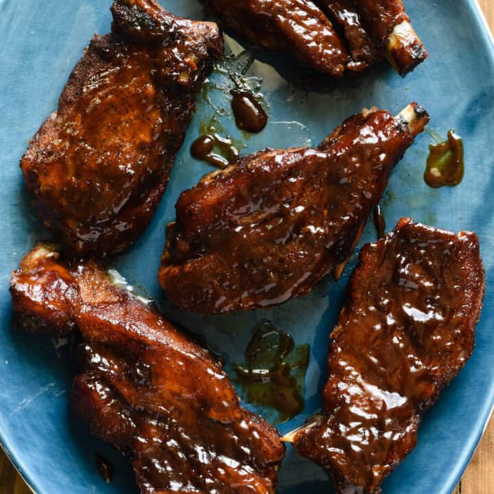 Country style pork ribs glazed with barbecue sauce on an oval shaped blue platter.