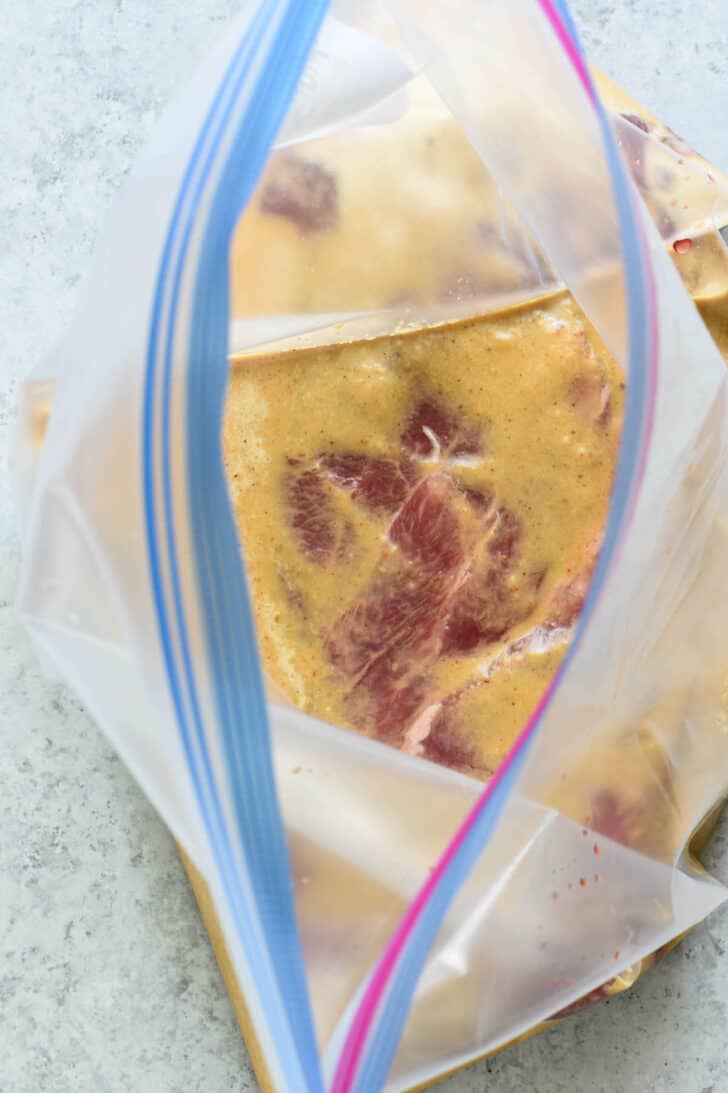 A raw flat iron steak covered in marinade in a zip top bag.
