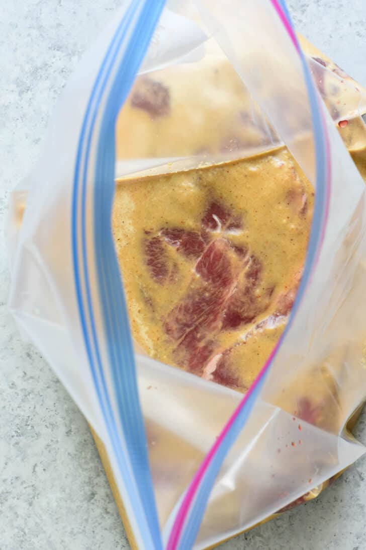 A raw piece of beef in a light brown liquid in a zip top bag.