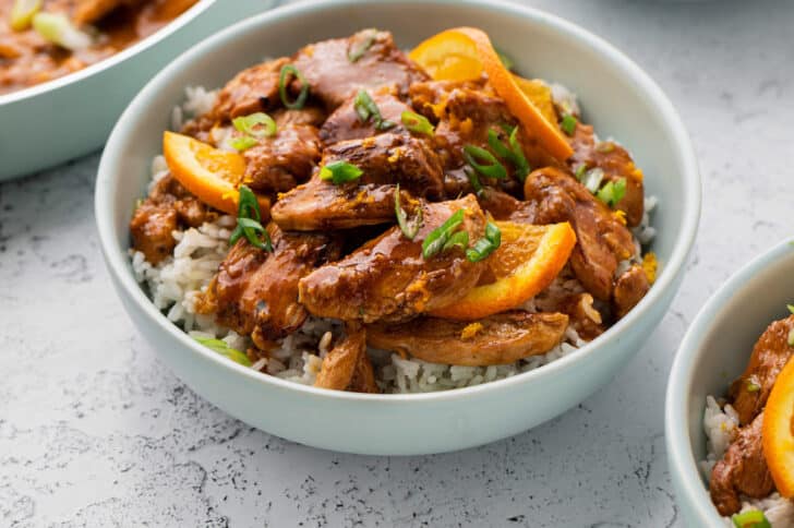 White rice topped with chicken with orange chicken marinade in a white bowl.