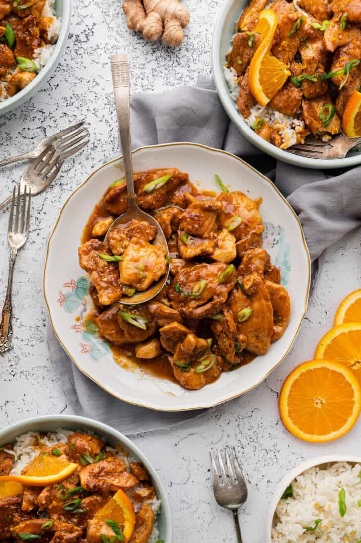 Plate with stir fried poultry and an orange chicken sauce recipe, garnished with green onions.